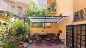 Eine Terrasse mit Tisch und Stühlen, umgeben von Topfpflanzen und einem Pflasterboden.