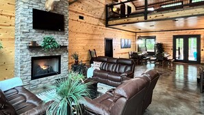 A spacious living room with a stone fireplace, leather sofas, and a high ceiling with exposed beams. - Hot Tub · Detached Game Rm · Pool Table | Dogs OK (Broken Bow)