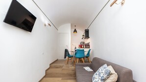 A narrow hallway with a wooden floor, a grey sofa with a patterned pillow, and a dining area with blue chairs and a table. - Rental in Rome Roma Campus Martius Apartment (Rome)