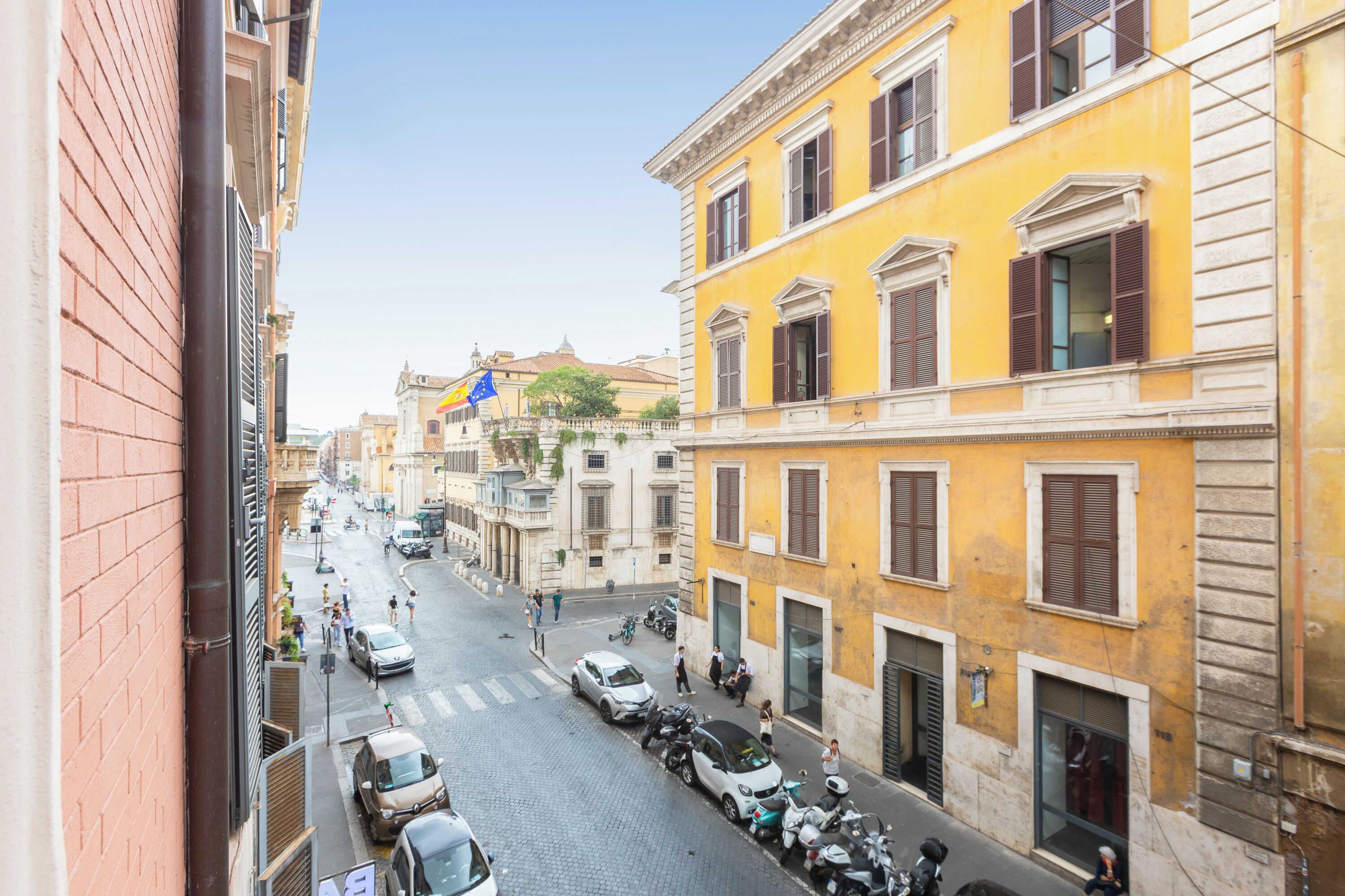 A street view with parked cars and a yellow building with classical architecture.