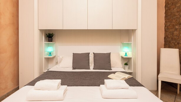 Une chambre d’hôtel avec un lit, deux tables de chevet avec des lampes, une chaise et une petite plante.