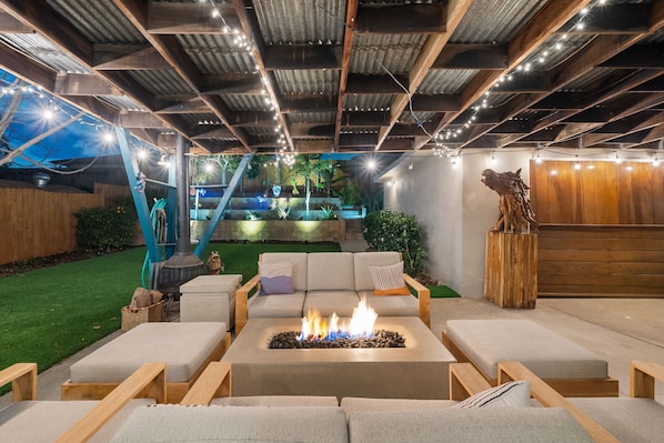 Un patio al aire libre con un brasero, asientos y vistas a un jardín ajardinado.