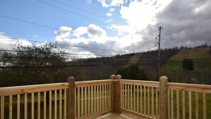 Eine Holzterrasse mit Geländer, die auf eine Wiese und eine hügelige Landschaft blickt.