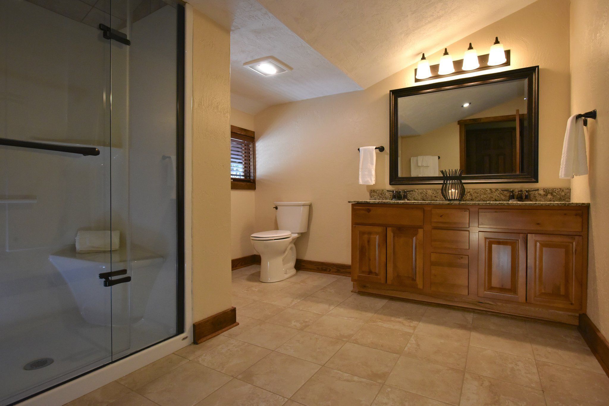Une salle de bain avec une douche à parois de verre, des toilettes, des meubles en bois et un grand miroir avec des lumières au-dessus.