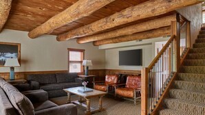 Una sala de estar acogedora con techo de madera, un conjunto de sofás, una mesita de centro y una escalera.