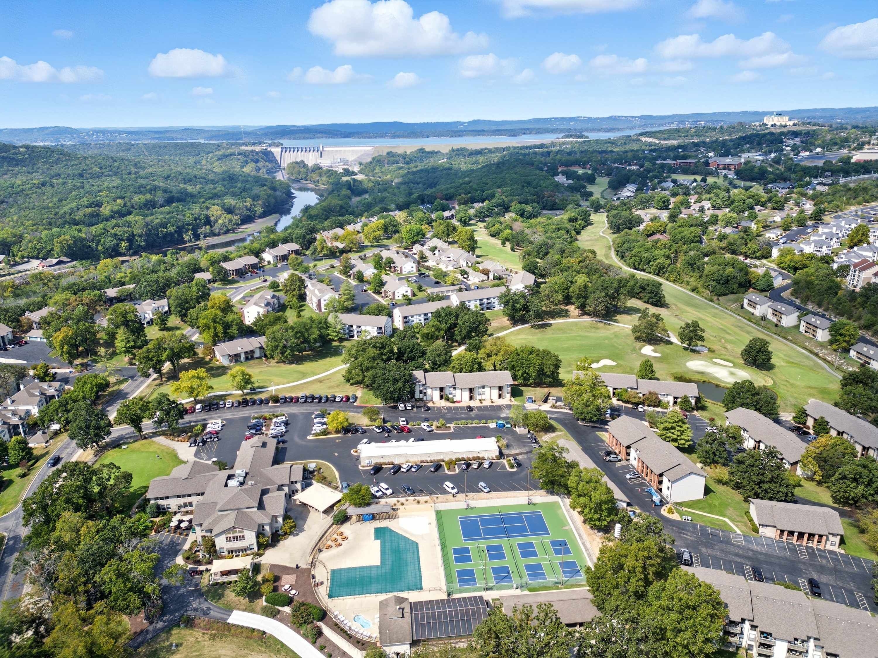 An aerial view of a residential area with a large swimming pool, tennis courts, and a golf course.