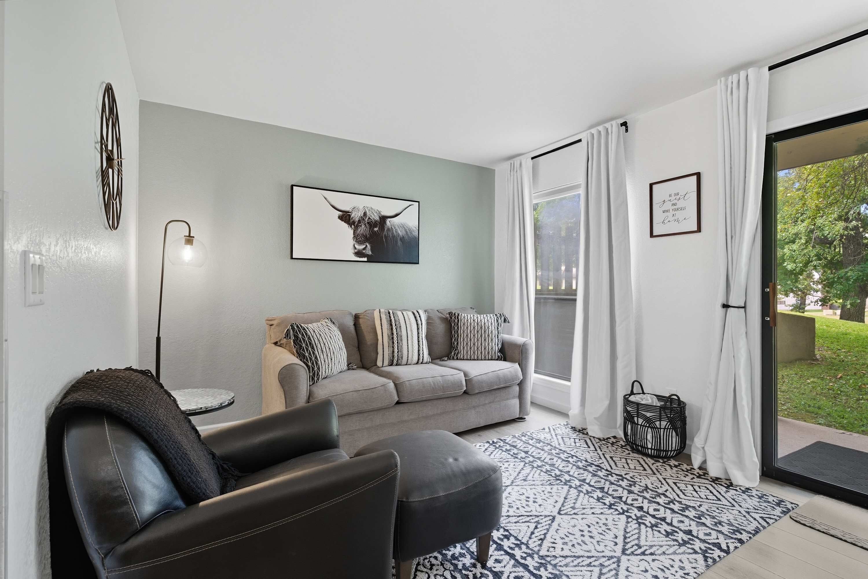 A modern living room with a grey sofa, black leather armchair, and a patterned rug.