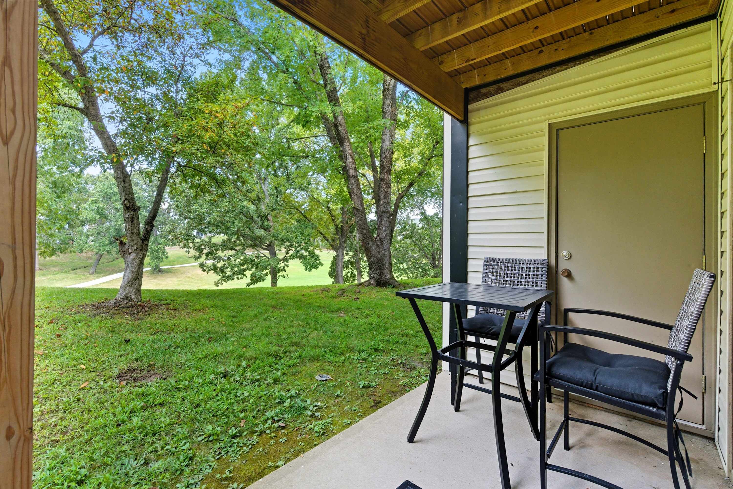 A covered patio with a table and chairs, a door, and a view of a grassy area with trees.
