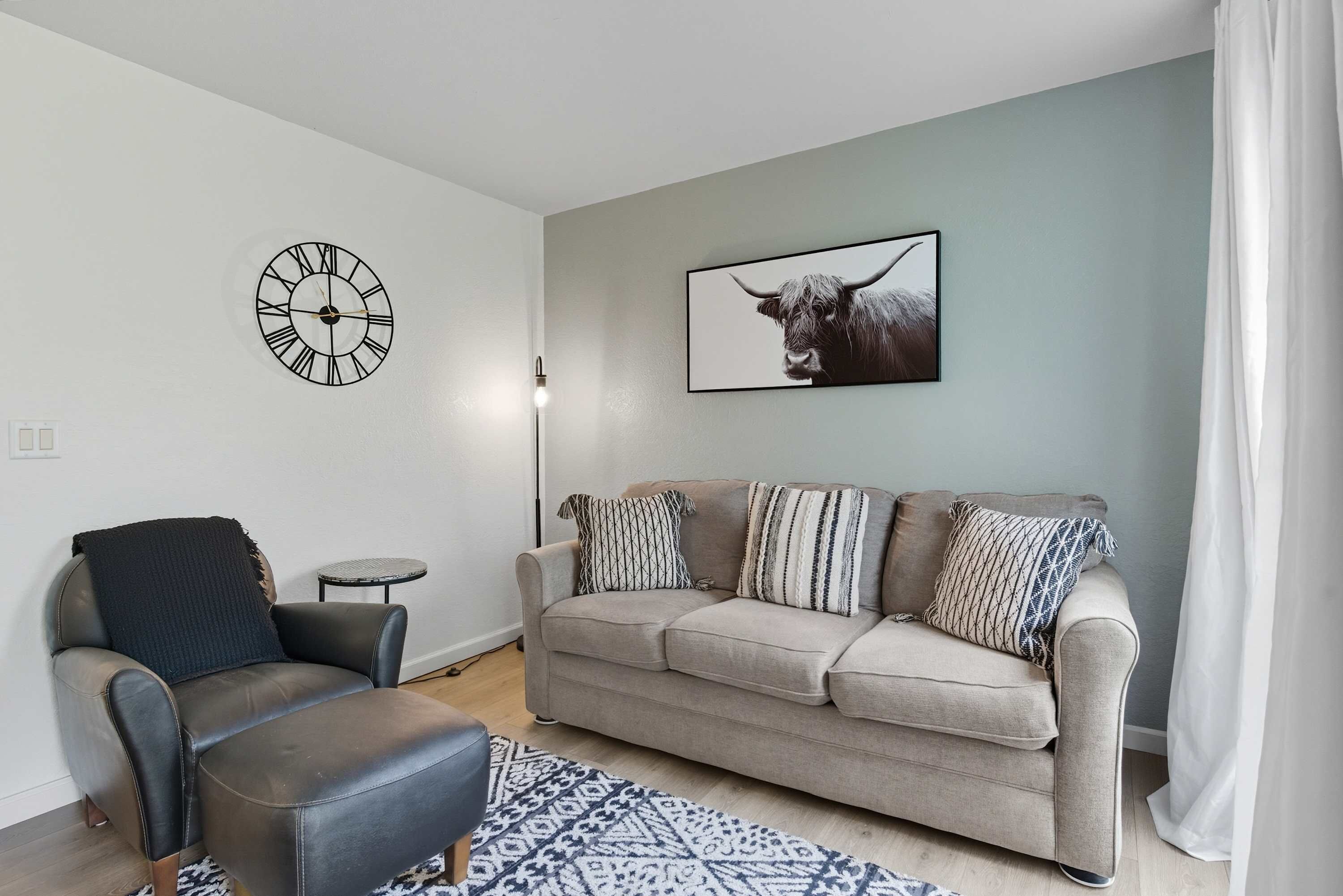 A living room with a sofa, armchair, and a clock on the wall.