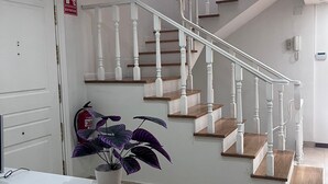 Una escalera con barandillas blancas, escalones de madera, un extintor y una planta en maceta.