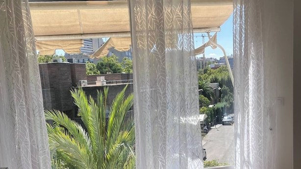 Un dormitorio con cama, cortinas y vistas a zonas verdes y edificios.