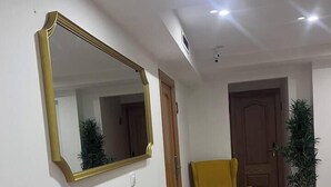 Un pasillo con un espejo grande, un sillón amarillo y una planta en maceta.
