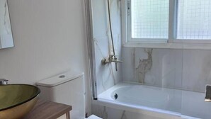 Un baño con bañera, inodoro, lavabo y una ventana con persianas.