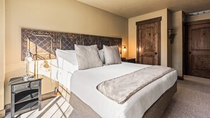 Una cama bien hecha con cabecera, una mesita de noche con lámpara y una puerta de madera en una habitación de hotel.
