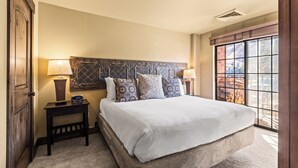 A bedroom with a large bed, two bedside tables with lamps, a decorative headboard, and a view through a large window. - 1 block from Park City Mountain with hot tub Managed by Park City Lodging (Park City)