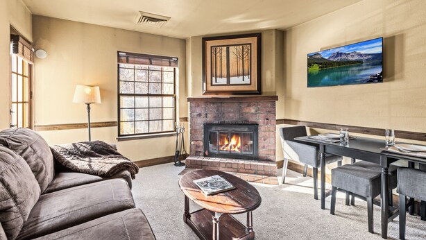 A living room with a fireplace, a sofa, a coffee table, a dining table with chairs, and a painting on the wall. - 1 block from Park City Mountain with hot tub Managed by Park City Lodging (Park City)
