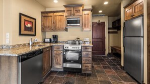 A kitchen with wooden cabinets, a stainless steel refrigerator, a built-in oven, and a granite countertop.