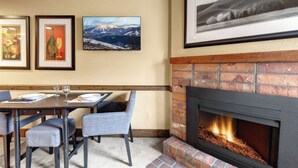A dining area with a brick fireplace, framed artwork on the wall, and a table set for two.