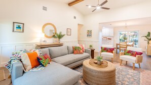A spacious living room with a grey sofa, colorful pillows, a round coffee table, and a ceiling fan. - Ibis Island Escape (Fort Myers Beach)