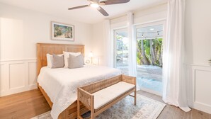 A bedroom with a large bed, a ceiling fan, a window with curtains, and a view of the outdoors. - Ibis Island Escape (Fort Myers Beach)