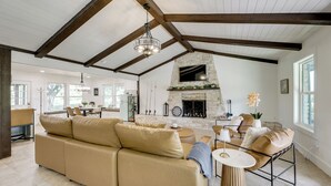 Ein geräumiges Wohnzimmer mit Kamin aus Stein, einem großen beigen Sofa und einem Essbereich mit Holztisch und -stühlen.