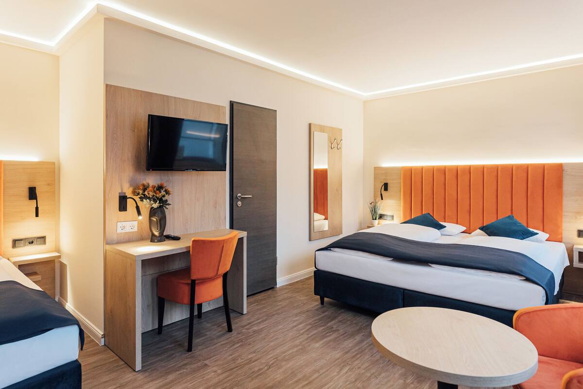 A modern hotel room with a bed, desk, chair, TV, and a round table.