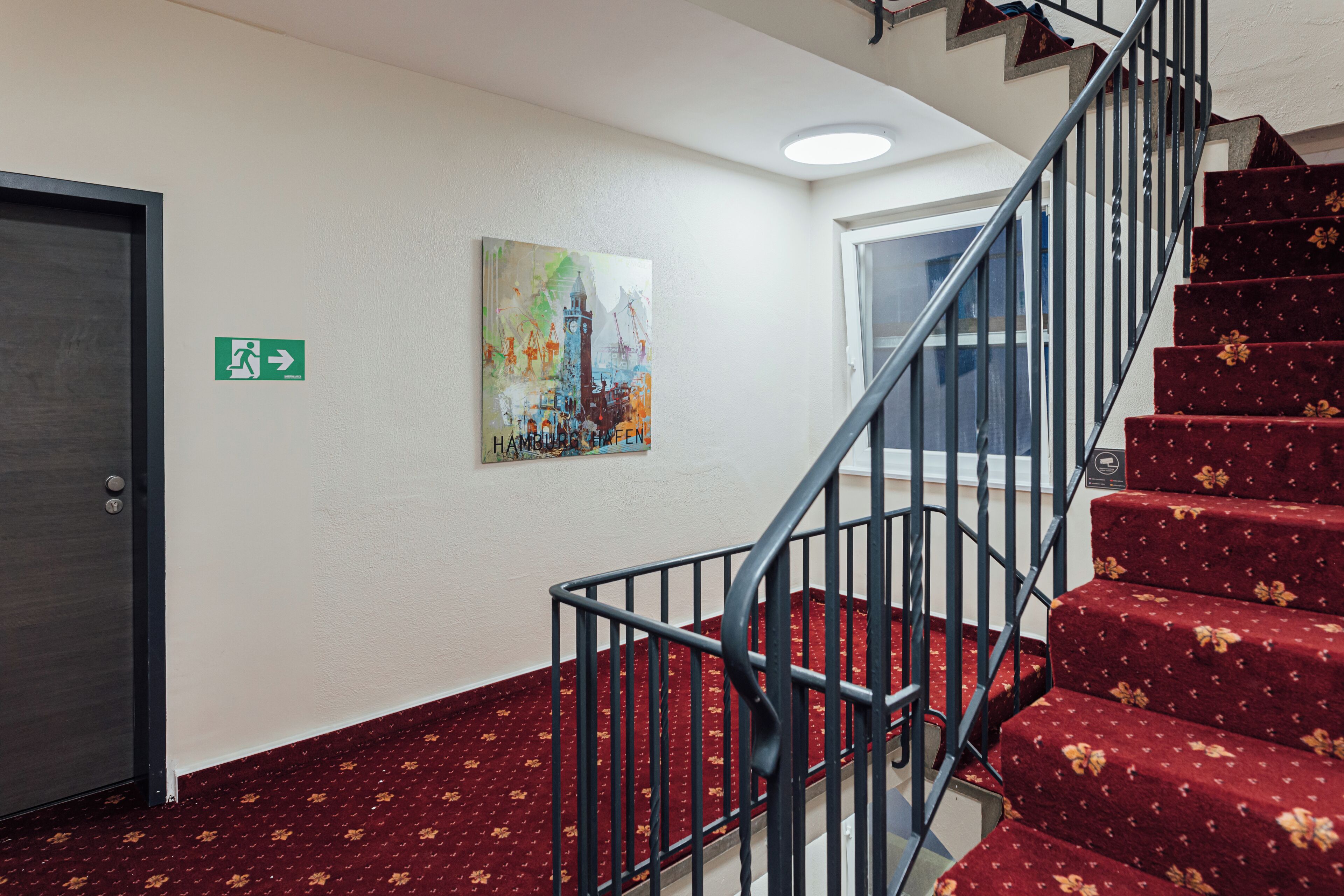 A staircase with red carpeted steps and a metal railing, leading to an upper floor.