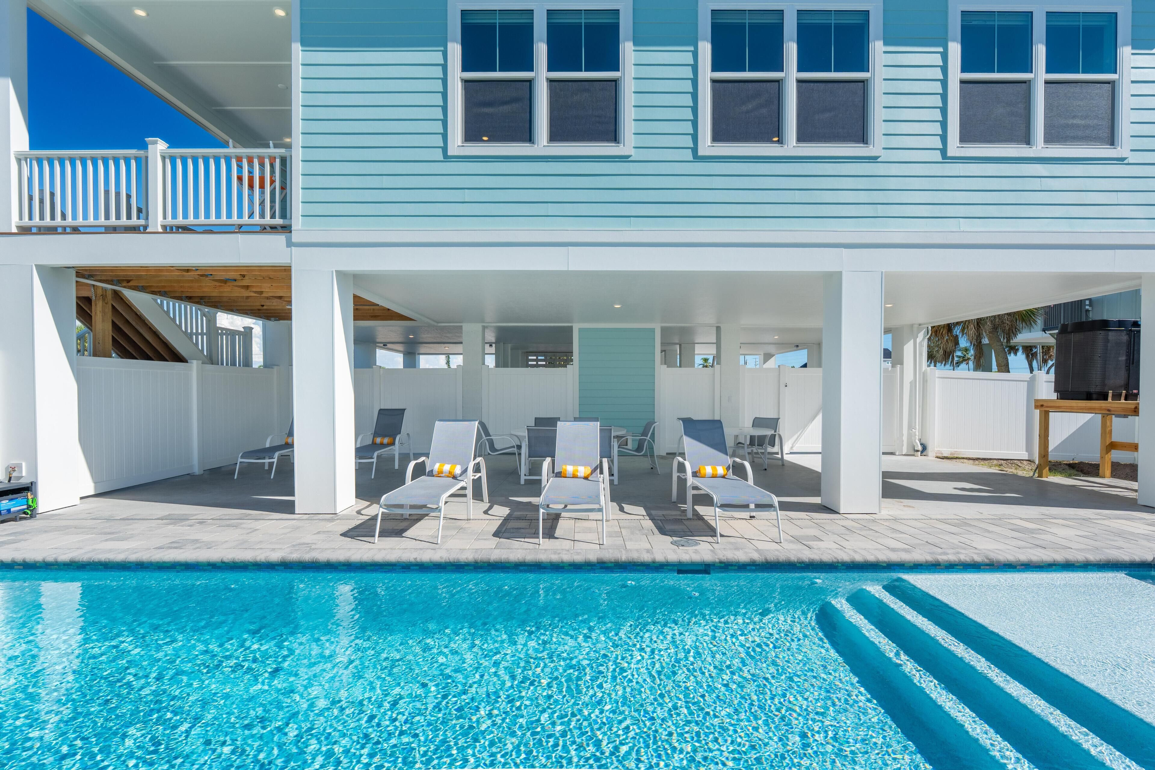 Ein zweistöckiges Haus mit Pool, Sitzgelegenheiten im Freien und einer überdachten Terrasse.