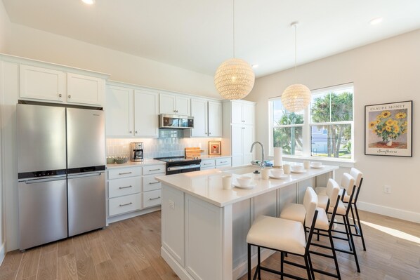 A modern kitchen with white cabinetry, stainless steel appliances, and a central island with bar stools.