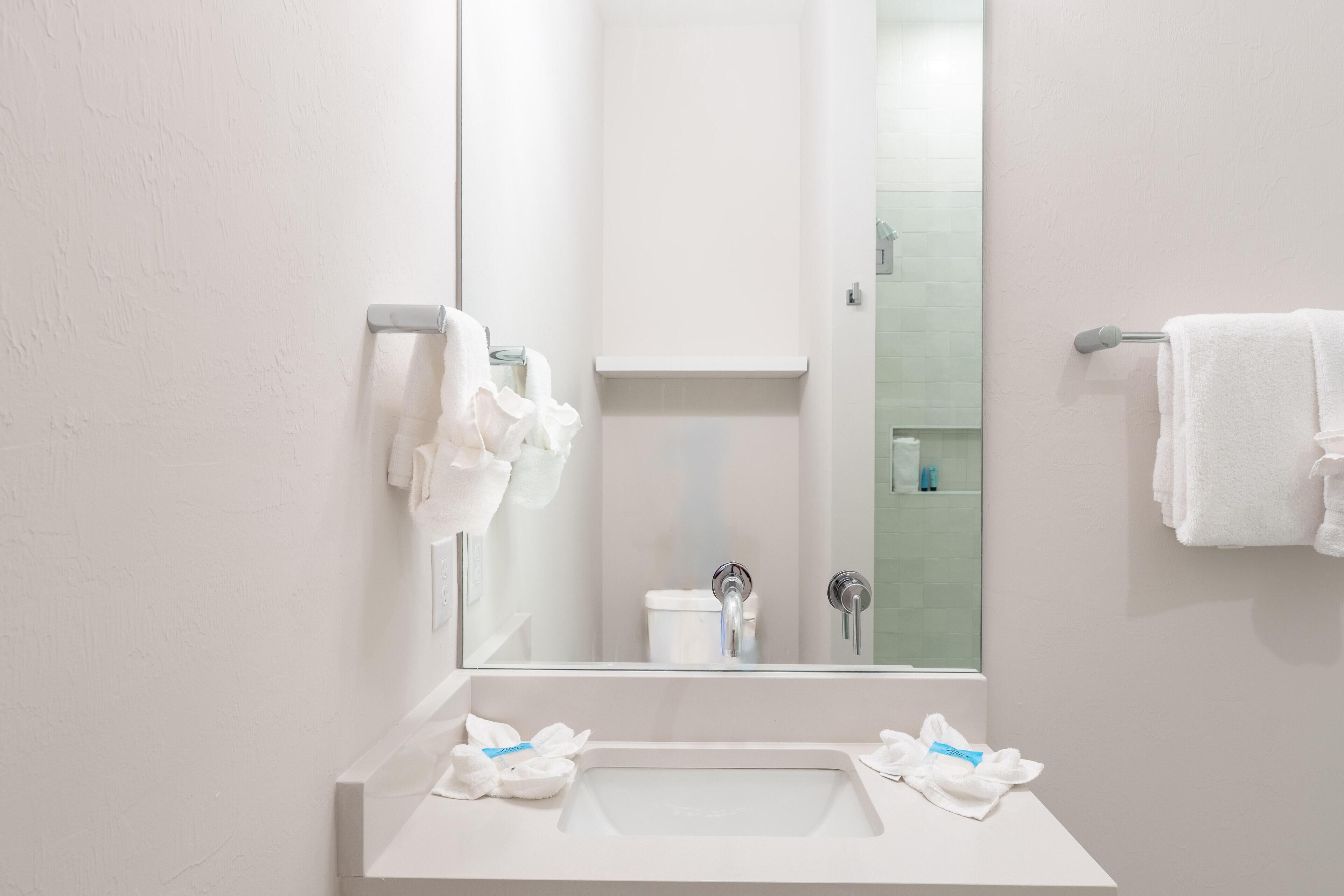 Ein modernes Badezimmer mit einem weißen Waschbecken, zwei Wasserhähnen und einem Spiegel.
