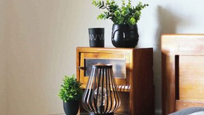 A neatly made bed with a white pillow and a gray blanket, a wooden nightstand with a potted plant, a black vase, and a decorative metal lamp. - Holiday cottage surrounded by vineyards (Zgornji Leskovec)