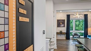 A modern lounge area with a black door labeled "THE VIBE LOUNGE," a seating area with a sofa and chairs, and a large window offering a view of greenery. - Upscale & Cool - Walk to Bars - Mins. to Broadway (Nashville)