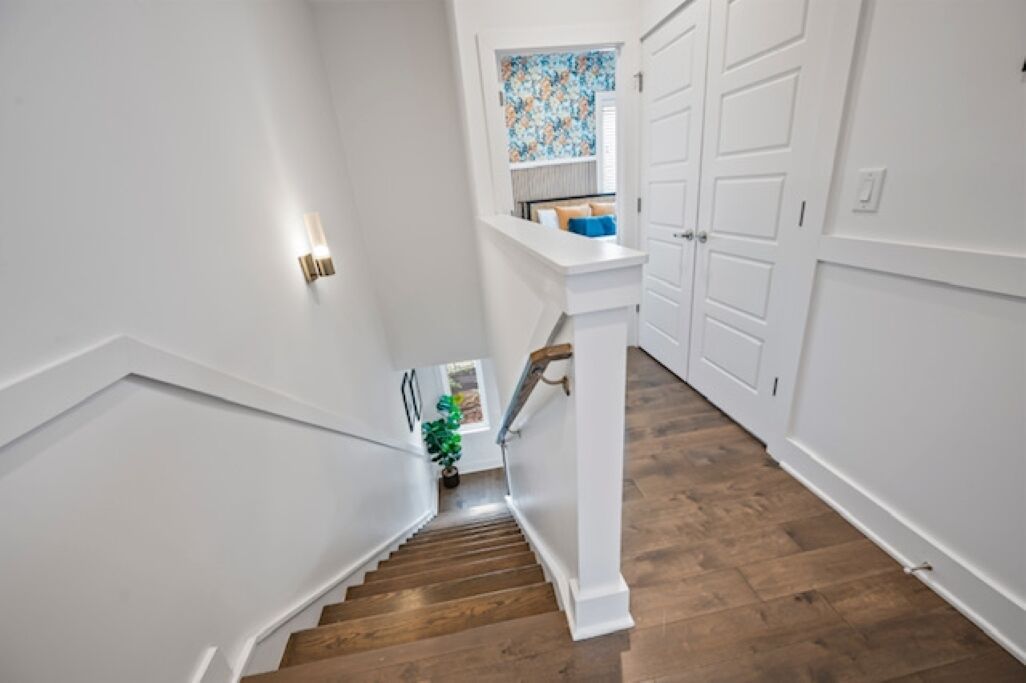 A staircase with wooden steps and white walls, leading to a room with a window and a door.