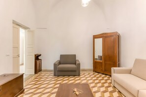 A living room with a sofa, armchair, wooden wardrobe, and a patterned floor.