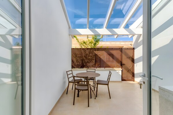 A balcony with a glass door, a round table with chairs, and a view of the cityscape through the glass.