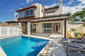 A two-story building with a swimming pool, outdoor seating, and a covered patio area.