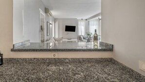 A modern kitchen with granite countertops, a flat-screen TV mounted on the wall, and a dining area with a table and chairs. - Vacation Villa 'La Caleta Seaside  with Pool' with Sea View, Wi-Fi and Air Conditioning (Adeje)