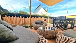 A patio area with wicker furniture, a table with a kettle and cups, and a wooden fence in the background.
