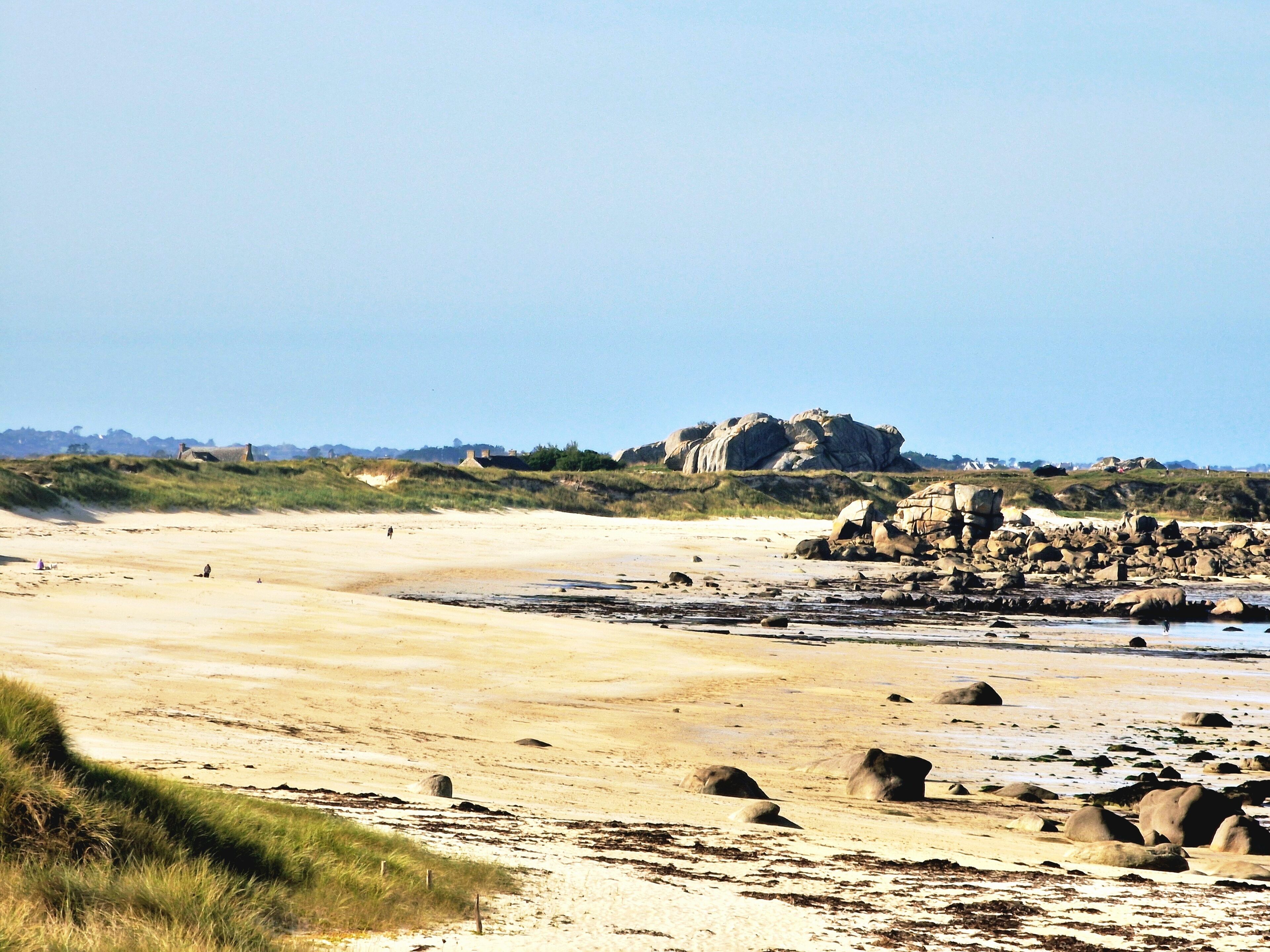 A sandy beach with scattered rocks and dunes.