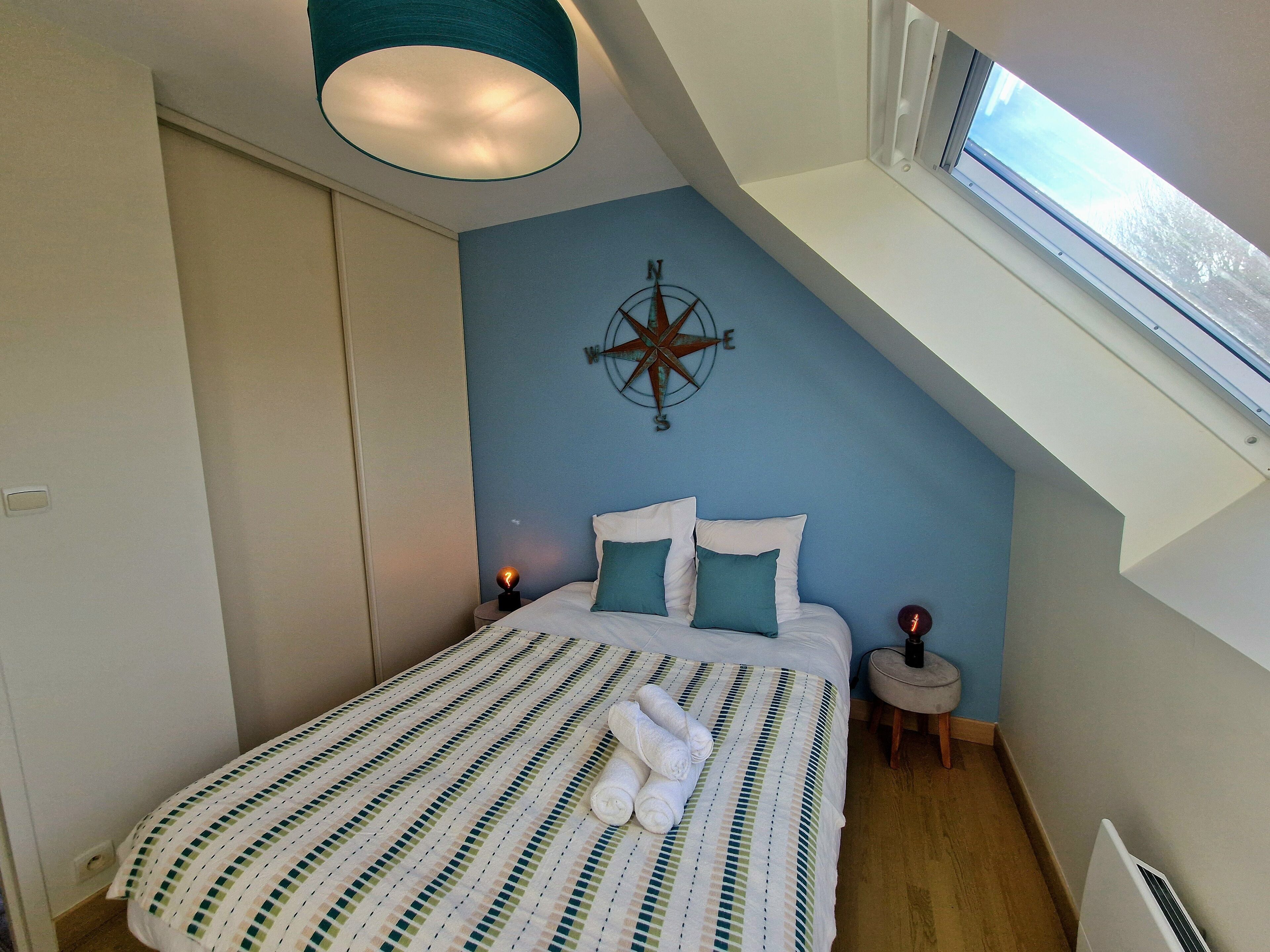 A bedroom with a sloped ceiling, a bed with striped bedding, a compass wall decoration, and a window.