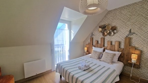 A bedroom with a sloped ceiling, a bed with striped bedding, a wooden headboard, bedside lamps, and a view through a window.