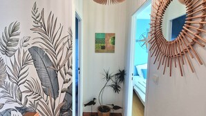 A hallway with a wooden staircase, a hanging light fixture, a wall-mounted mirror, and a potted plant.