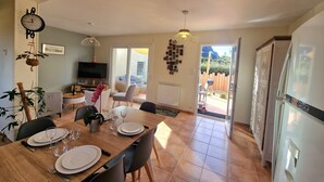A dining area with a wooden table set for four, a television, and a plant.