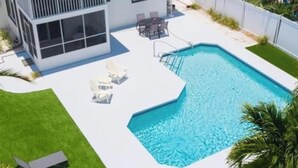 Une maison moderne à deux étages, dotée d’une piscine, d’une terrasse avec des chaises et d’une pelouse bien entretenue.