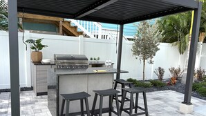 Une cuisine extérieure équipée d’un barbecue, de tabourets de bar et d’un patio couvert.
