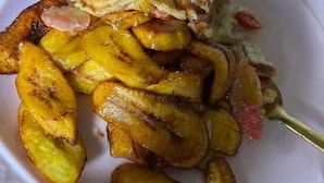 Une assiette contenant des bananes plantains frites, des œufs brouillés et des oignons en tranches.
