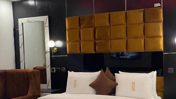 Une chambre d’hôtel moderne avec un grand lit, une tête de lit au motif capitonné et un miroir avec un cadre en marbre.
