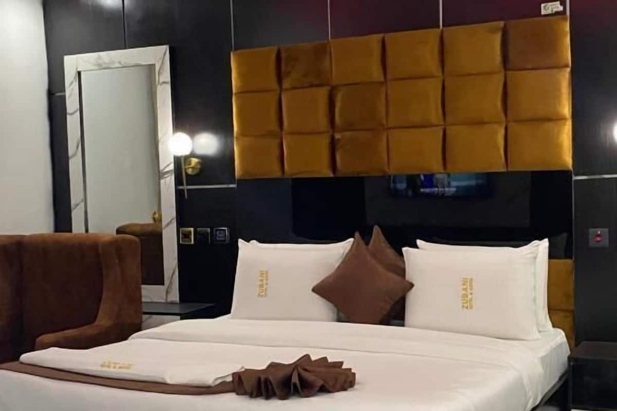 Una habitación de hotel moderna con una cama grande, un cabecero con diseño capitonado y un espejo con marco de mármol.