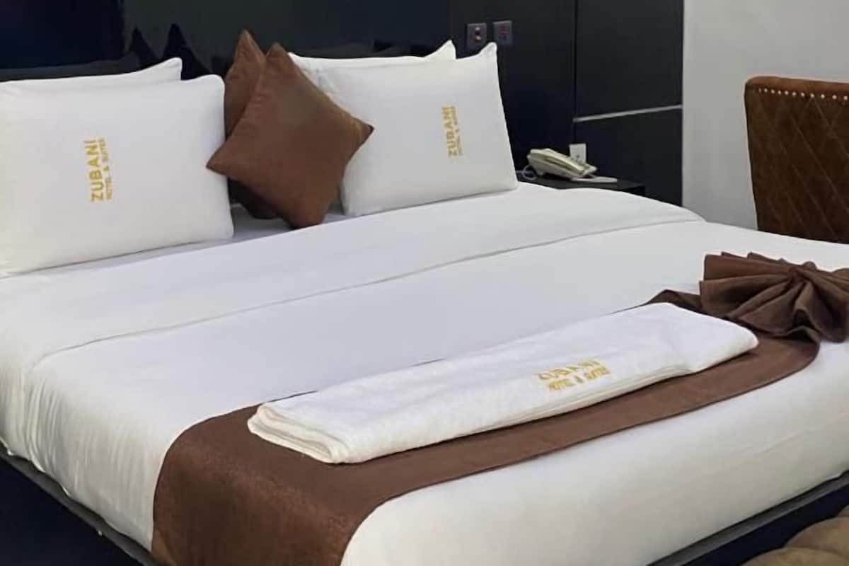 Habitación de hotel con una cama grande, cabecera, mesita de noche y lámpara de pared.