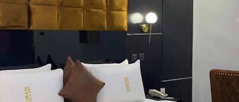 A hotel room with a large bed, a headboard, a nightstand, and a wall-mounted lamp.